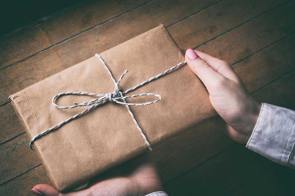 Mujer tiene entre sus manos un regalo envuelto con un lazo.