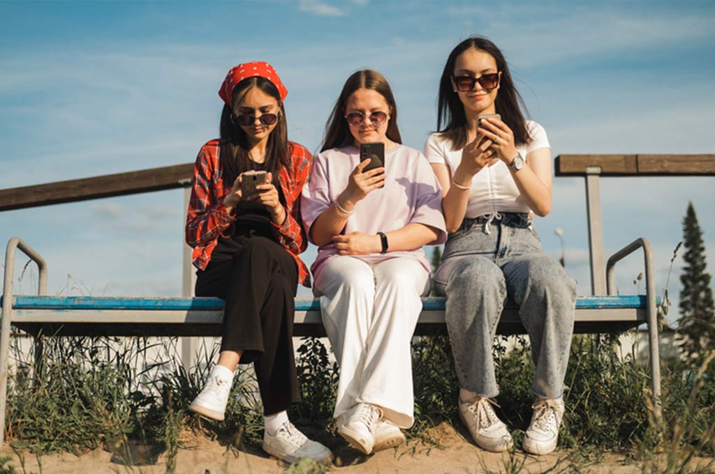 Young women sitting on a bench looking at their phones.